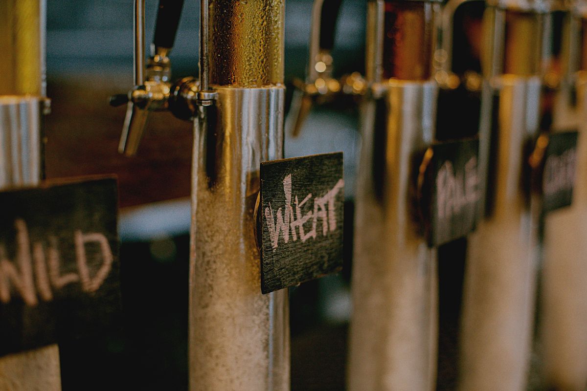 Cold stainless-steel beer taps with condensation and chalkboard labels reading Wild, Wheat, Pale and Cider